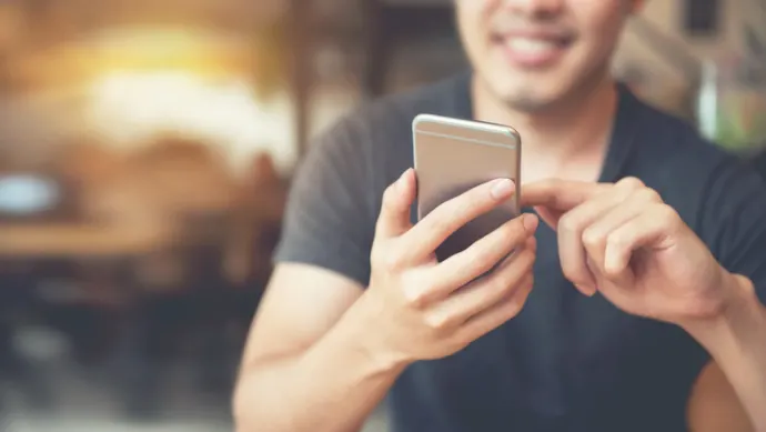 Man smiling and holding cellphone and reading text message. 